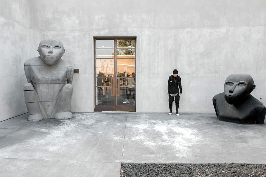 person standing beside statues, man standing beside gray wall between statues HD wallpaper