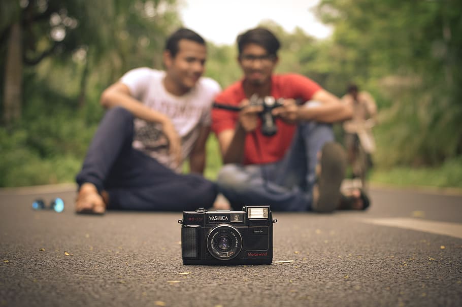 black camera in front of two men sitting on road, analog camera HD wallpaper
