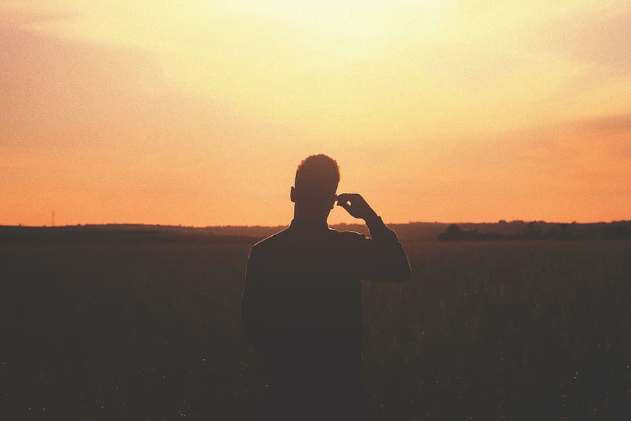 silhouette of person standing on field during golden hour, man