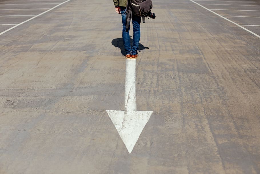 person standing on arrow sign on road, person standing on gray and white concrete pavement with arrow HD wallpaper