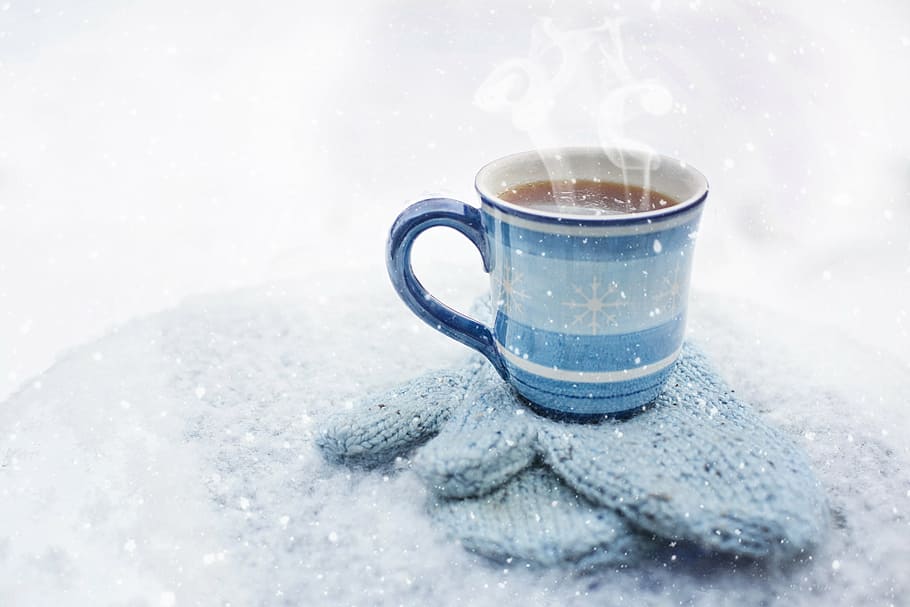 ceramic mug on knitted gloves with hot liquid, coffee, winter