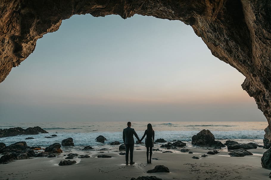 man and woman holding hands facing sea, man and woman standing next to each other near shore HD wallpaper
