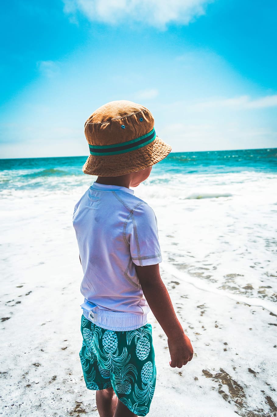 Brother Views, child wearing white t-shirt, green and white pineapple print shorts and khaki bucket hat over white sand seashore across wavy body of water during daytime HD wallpaper
