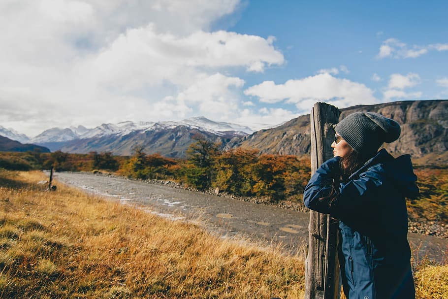 woman wearing blue jacket leaning on brown wooden post, person standing beside brown post during daytime HD wallpaper