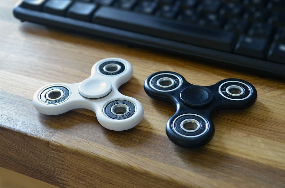 two fidget spinners on desk near keyboard, toy, hand, stress HD wallpaper
