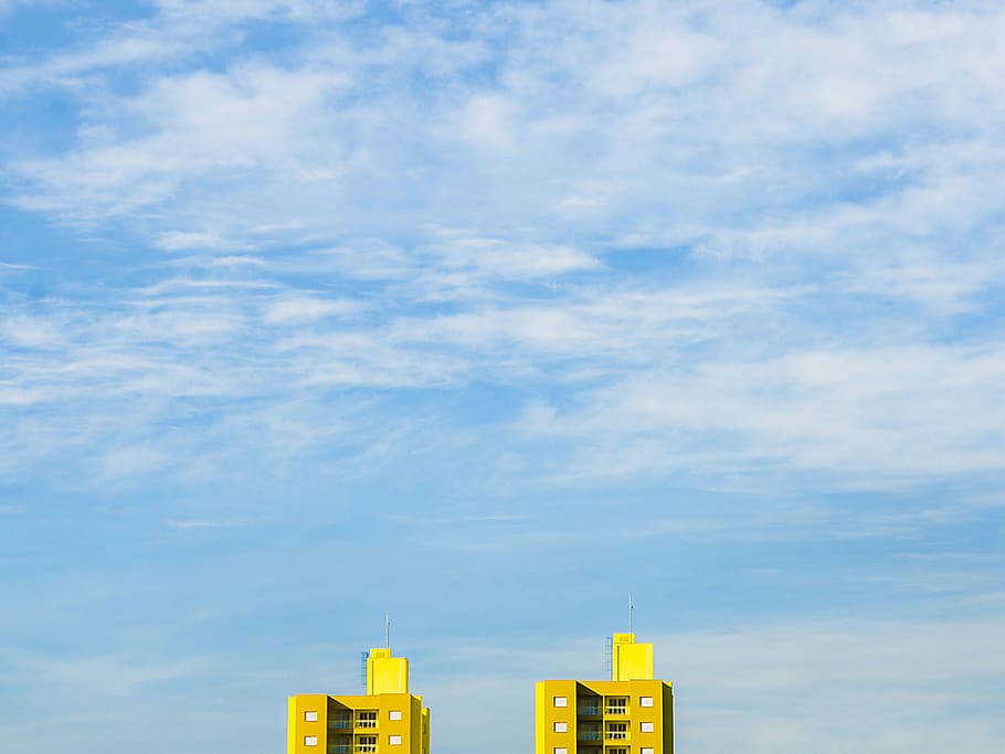 close up photography of two yellow buildings, two yellow concrete buildings under white cloudy sky at daytime HD wallpaper