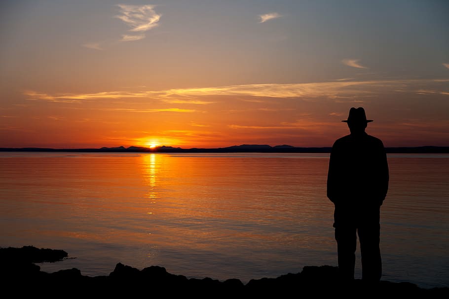 silhouette of man standing facing body of water, galway bay, sunset