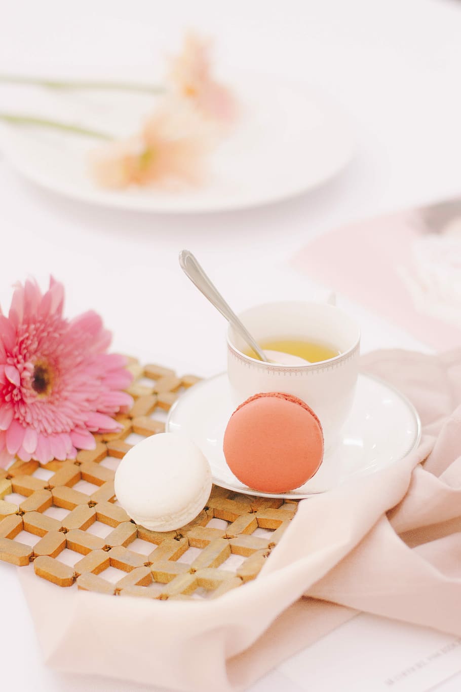 two orange and white macaroons beside white ceramic cup with spoon, two french macarons near white ceramic coffee cup and pink petaled flower HD wallpaper