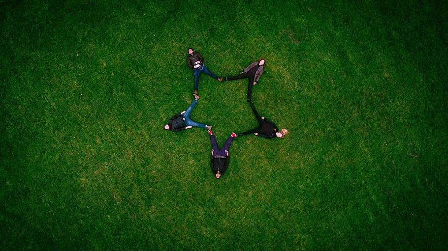 five people laying on grass field making star sign, five people laying on green landscape photgraphy