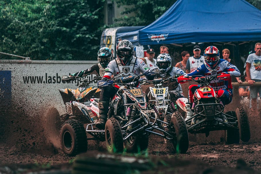 four men riding ATVs racing on mud with people watching during daytime, four persons riding on ATV quad bikes