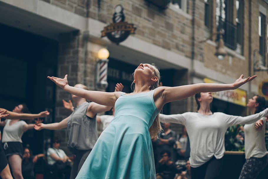 people dancing on street at daytime, woman stands with wide arms open in between buildings HD wallpaper