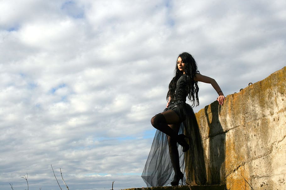 woman wearing black gown standing beside concrete wall under cloudy sky during daytime HD wallpaper