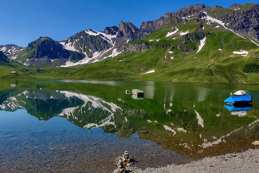 blue boat on bodies of water near mountain under blue sky at daytime, calm body of water near mountains HD wallpaper