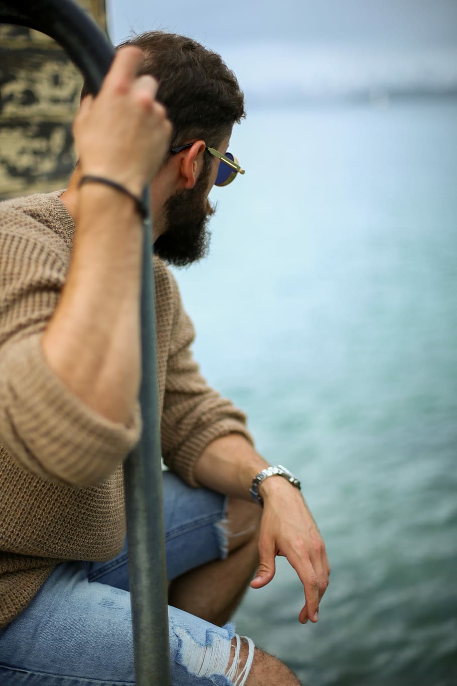 man sitting on while holding metal rail near ocean water, man holding a handrail while watching the ocean HD wallpaper