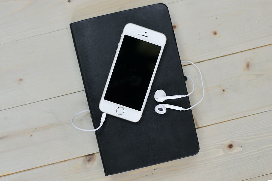 silver iPhone 5s with EarPods on top of black notebook, desk