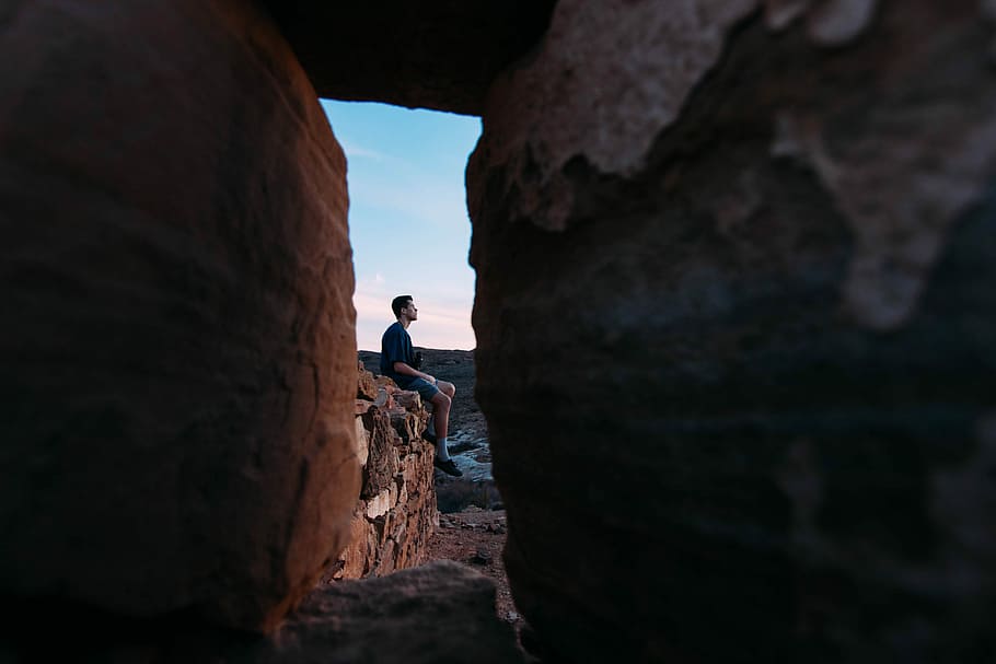 Man seated on red rocks, man sitting on during daytime, rocky HD wallpaper