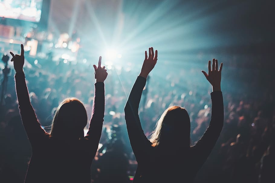 two woman standing on field of people, focus photography of two women raising both hands front of concert HD wallpaper