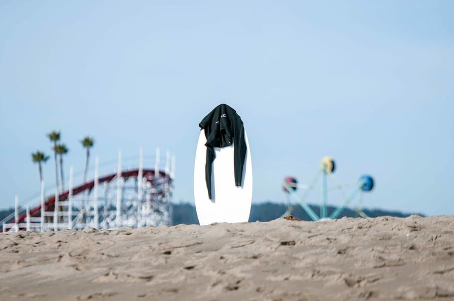 white surfboard with black rashguard on top in the middle of sand, white board with black shirt on brown sand HD wallpaper