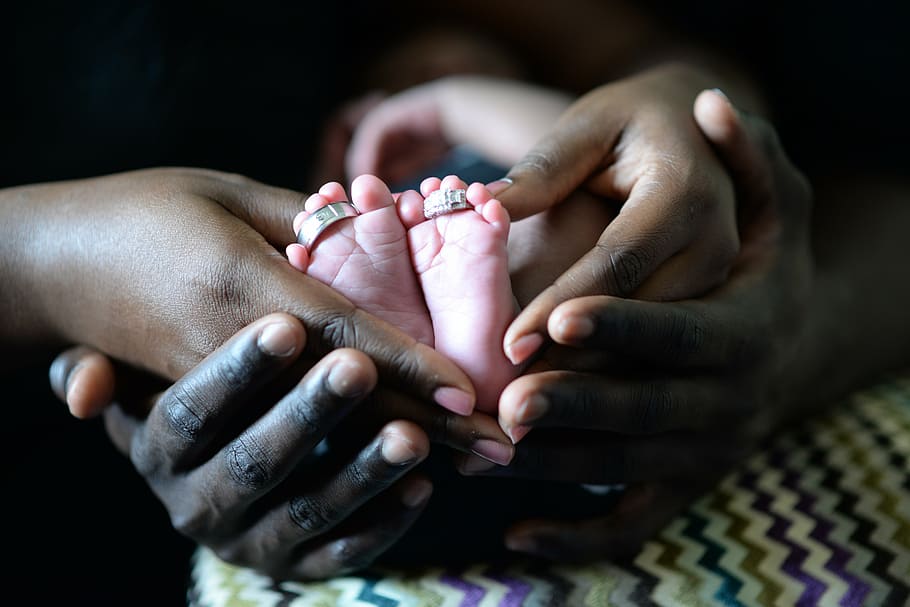 two adult hands with baby feet, couple, wedding rings, woman