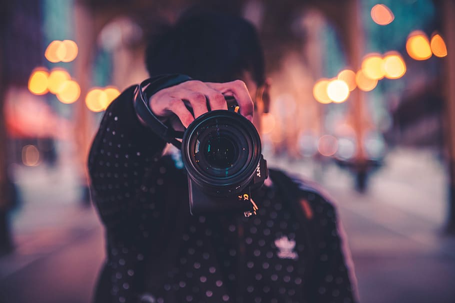 man holding black DSLR camera, man in black jacket holding black DSLR camera HD wallpaper