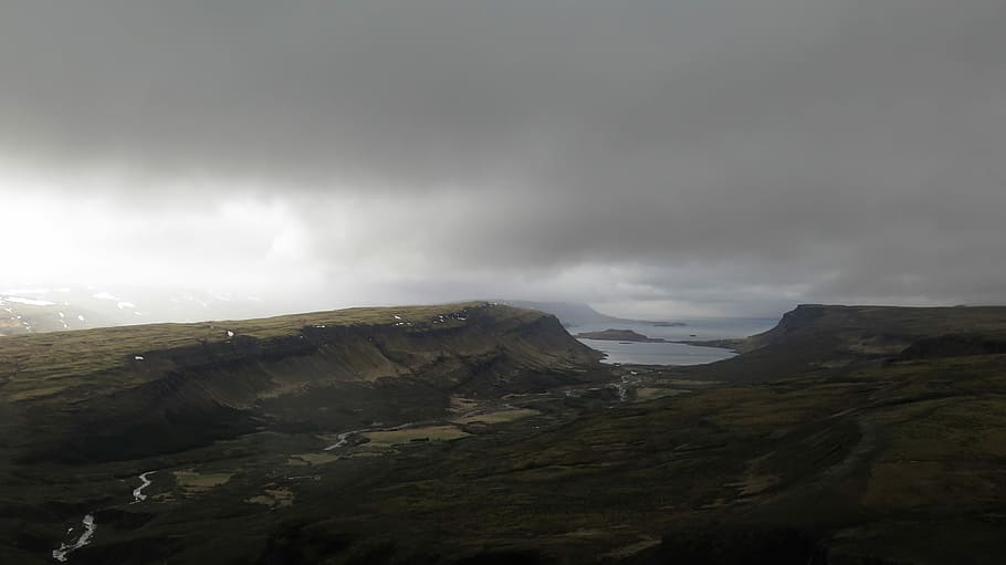 aerial photo of plain under gray cloudy sky at daytime, mountain near to body of water HD wallpaper