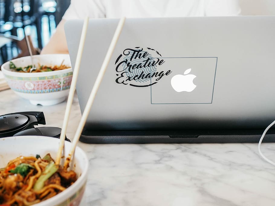silver MacBook near white bowl, person using MacBook beside bowl of noodles on white marble table, HD wallpaper