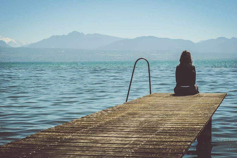 woman in black top sitting on brown wooden dock under blue sky during daytime HD wallpaper
