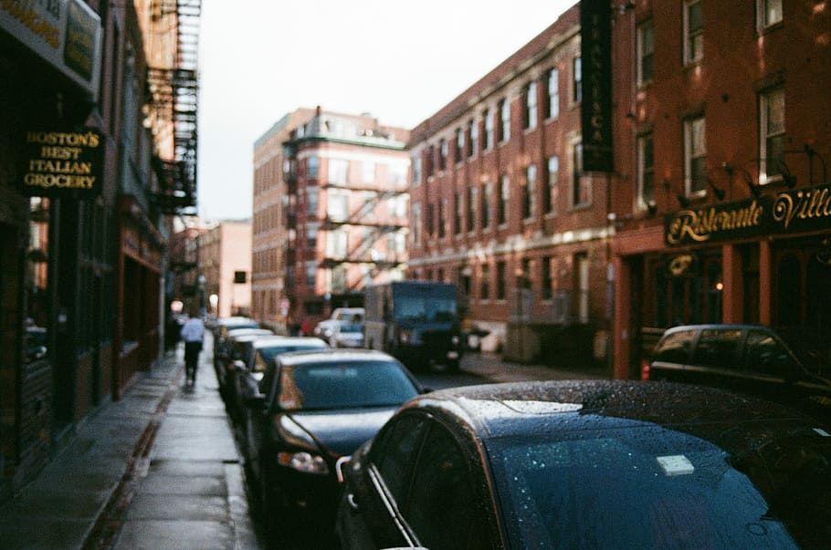 cars parked between highrise buildings under cloudy sky at daytime HD wallpaper