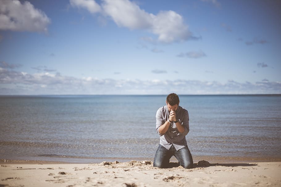 man wearing grey shirt kneeling down on beach shore praying under cloudy sky, HD wallpaper
