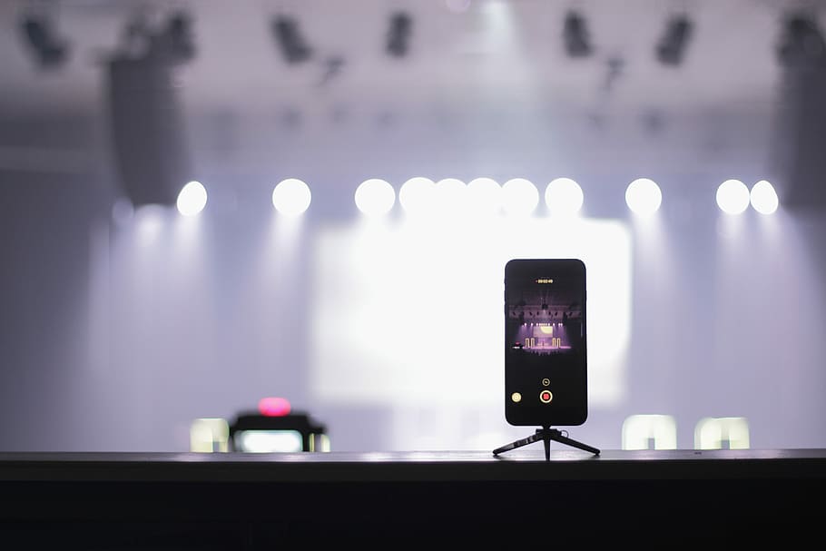 selective focus photography of iPhone displaying theater, phone placed on stage with stand while recording HD wallpaper