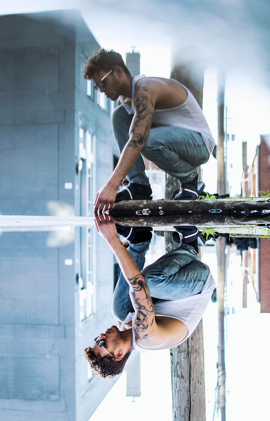 man squatting on stone near puddle casting his reflection, photo of man wearing white tank top HD wallpaper