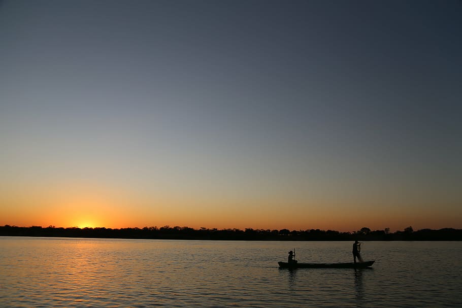two person riding boat on calm body of water during golden hour in silhouette photography HD wallpaper