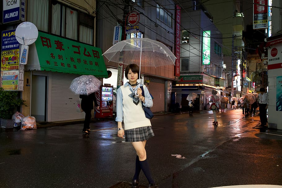 woman holding clear umbrella wearing white and blue collared long-sleeved shirt with black and gray plaid mini skirt standing surrounded by buildings during night, HD wallpaper