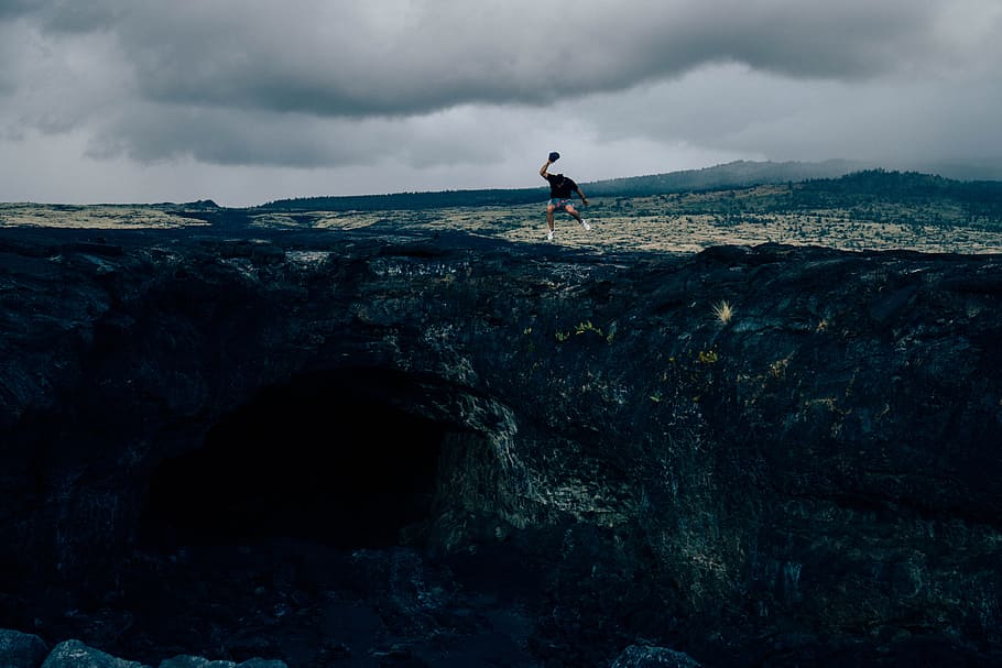 man standing on rock formation during daytime, man in black shirt jumped on brown cliff HD wallpaper