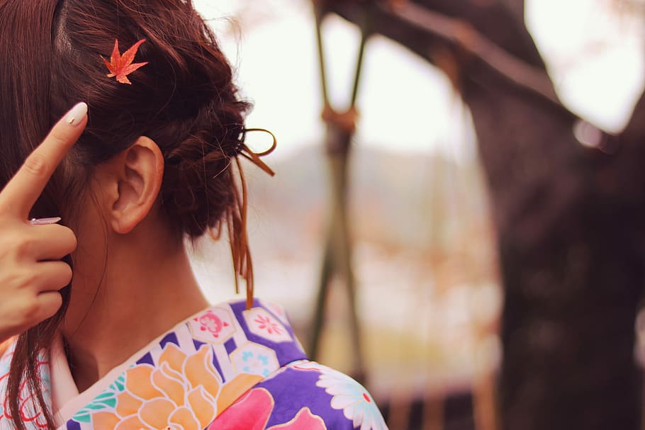shallow depth of field photo of woman in purple, pink, and orange floral shirt with red maple leaf hair clip HD wallpaper