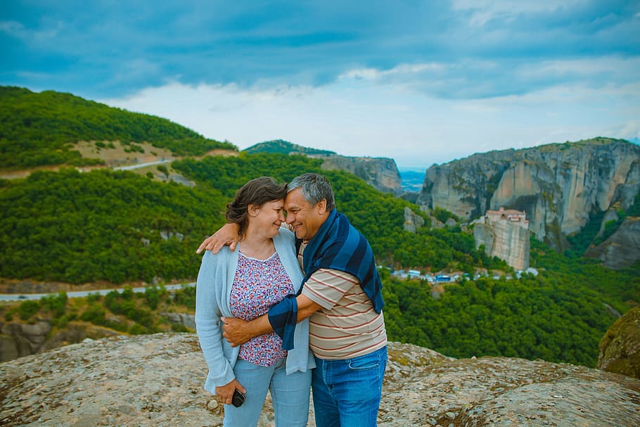 man embracing the woman on top of hill, couple standing on mountain top overlooking grass-covered mountains