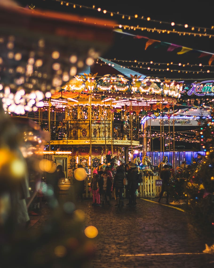 bokeh photo of carousel, people standing in amusement park during nighttime