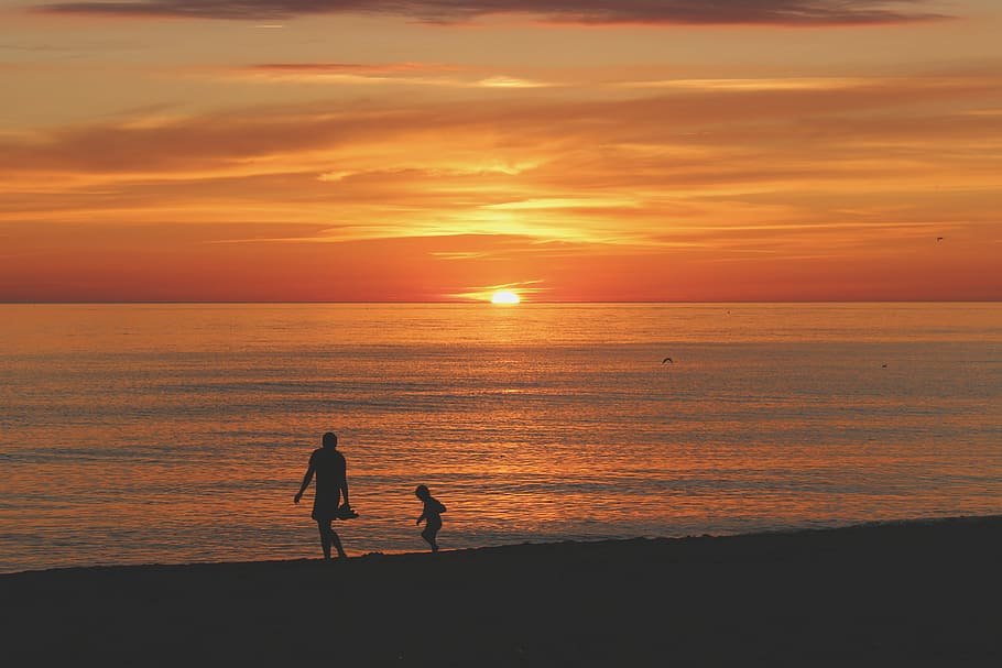 silhouette photo of two person walking on seashore near sea under orange sky during golden hour HD wallpaper