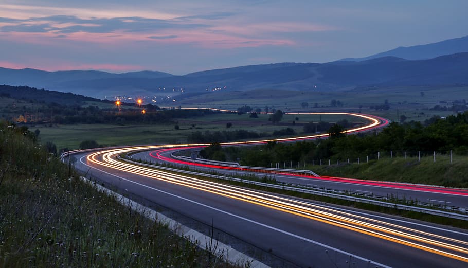 time lapsed photography of asphalt road, lighted winding concrete road at middle of green grass field HD wallpaper