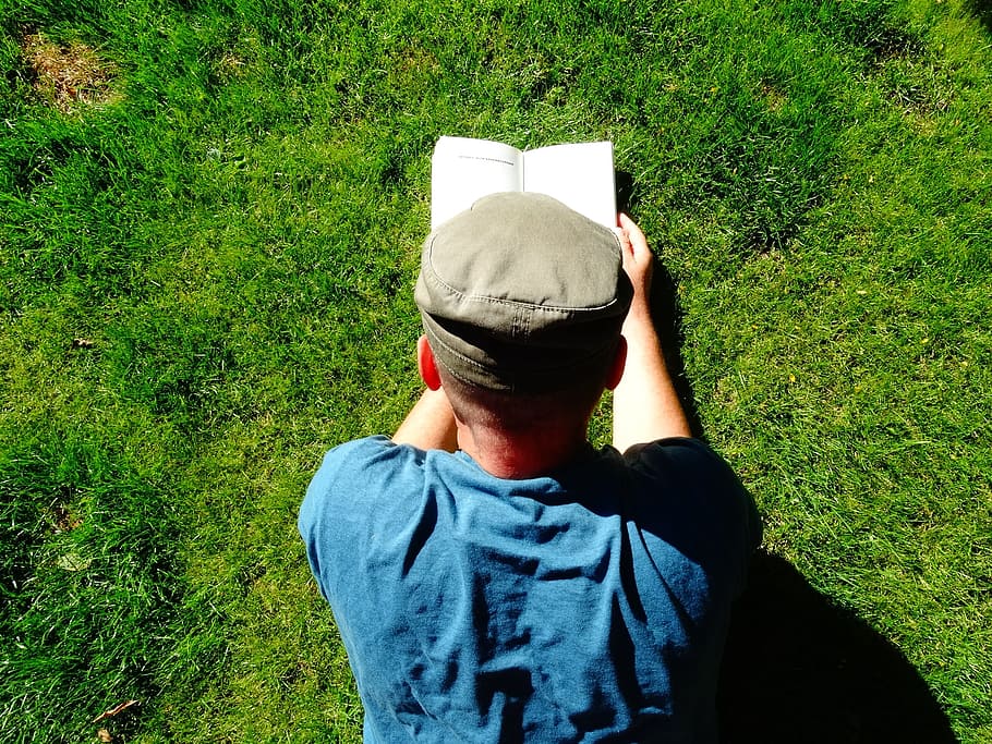man lying on green grass while reading book during daytime HD wallpaper