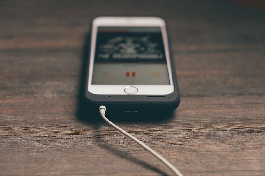 silver iphone with black case on brown surface, turned on iPhone displaying music on brown wooden surface HD wallpaper