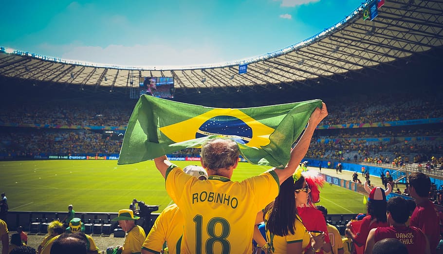 photo of man raising flag of Brazil on sports stadium, people
