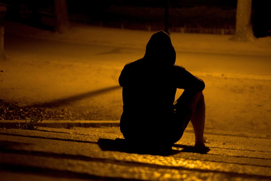 silhouette of person sitting on pathway during nighttime, man