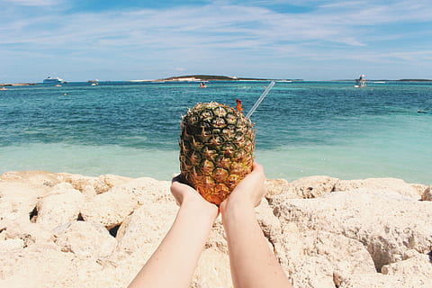 person holding pineapple on seashore during daytime, person holding pineapple with straw on beach shore HD wallpaper