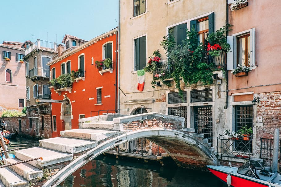 concrete bridge beside white building, landscape photography of gray concrete river bridge near red powerboat HD wallpaper