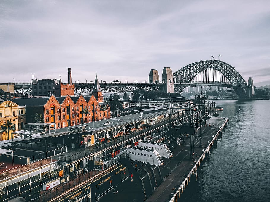 aerial photography of concrete buildings and bridge beside ocean under cloudy sky, photo of dock near body of water and suspension bridge HD wallpaper