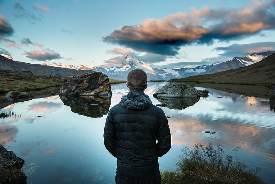 man in black jacket standing in front of body of water during daytime HD wallpaper