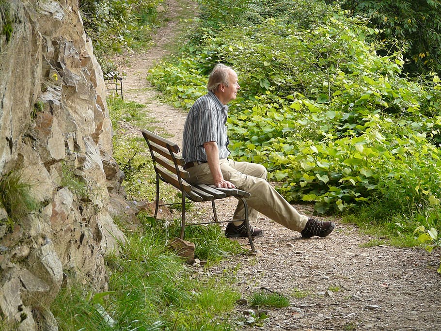 man sitting on brown wooden bench in front of beige stone, hike.
