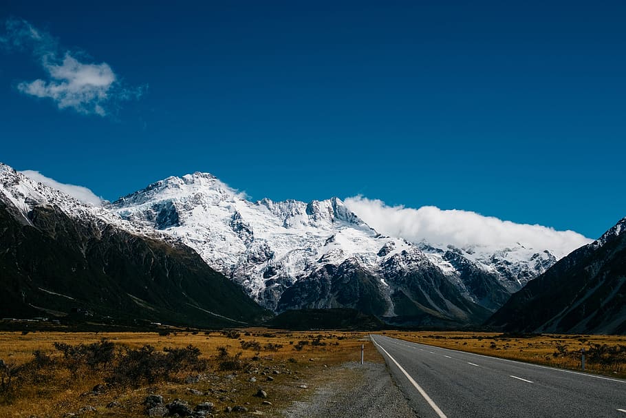 road toward mountain with snow at daytime, gray concrete road in between brown sands near gray mountain at daytime HD wallpaper