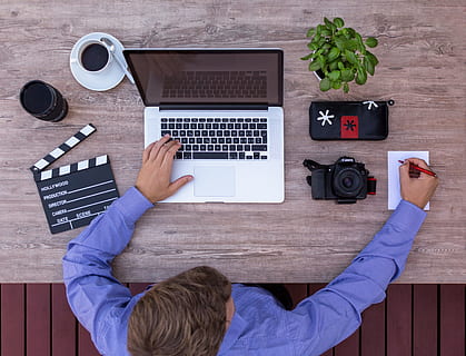 person writing on paper with MacBook Pro on table, filmmaker HD wallpaper